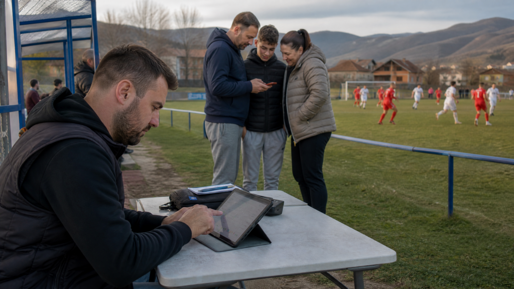 Zapisničar uz teren unosi događaj na tabletu dok publika prati utakmicu tokom lokalnog nogometnog turnira